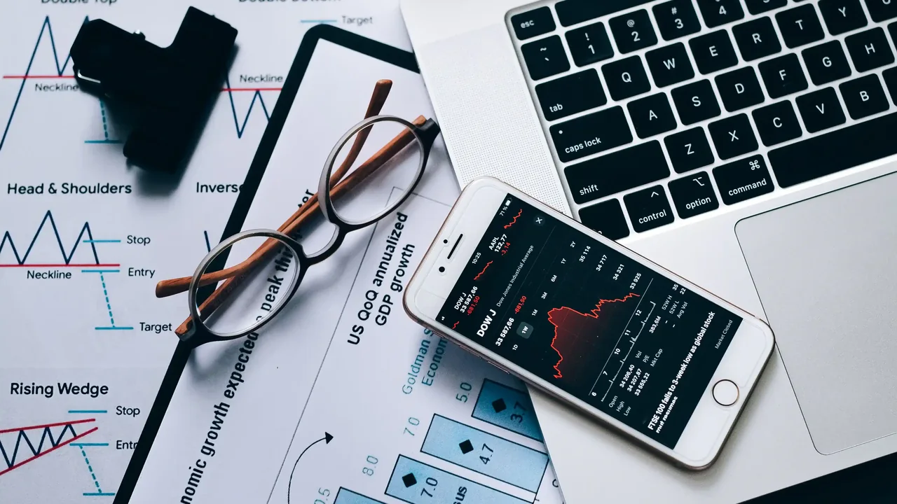 Research documents, charts, and a phone next to a laptop during an investment research review