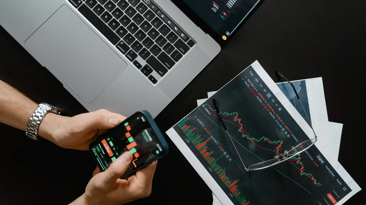 An investor reviewing a stock chart on a phone with printed market charts on a desk