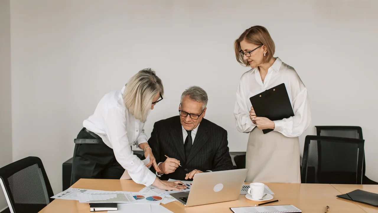 Professionals reviewing financial documents around a laptop during an investment meeting